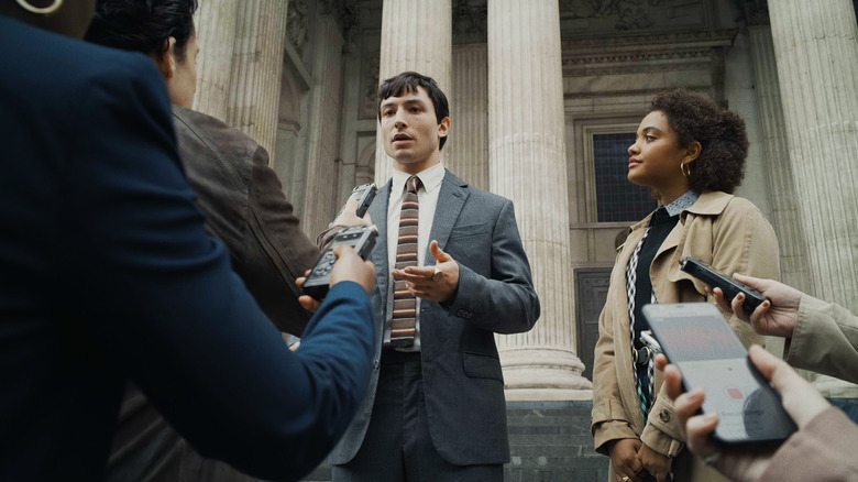 Ezra Miller's Barry Allen answers questions from reporters on some steps in The Flash