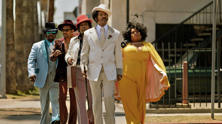 Eddie Murphy como Rudy Ray Moore, andando pela rua com sua comitiva dos anos 1970