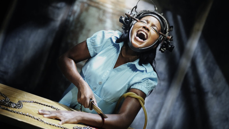 Simone, with a metallic death contraption strapped to her head, a rubber tube tied around her bicep, screaming as she sliced into her forearm with a hunting knife. A scene from Saw VI.