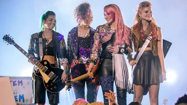Aja (Hayley Kiyoko), Shana (Aurora Perrineau), Jem (Aubrey Peeples), and Kimber (Stefanie Scott) standing onstage in Jem and the Holograms