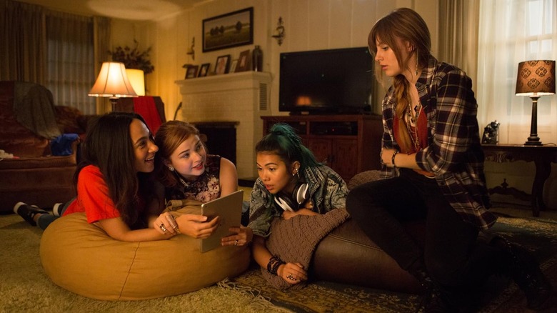 Shana (Aurora Perrineau), Kimber (Stefanie Scott), Aja (Hayley Kiyoko), and Jem/Jerrica (Aubrey Peeples) sitting in their living room in Jem and the Holograms