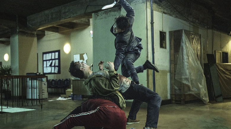 A man jumps and attacks Navin with a knife, while another man is crouched behind Navin in The Furious