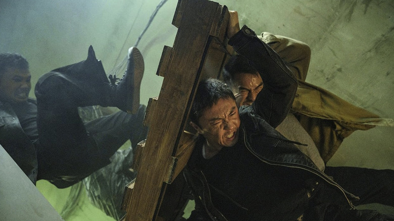 Wang Wei and Navin use a wooden palette as a shield from a man kicking at them in The Furious