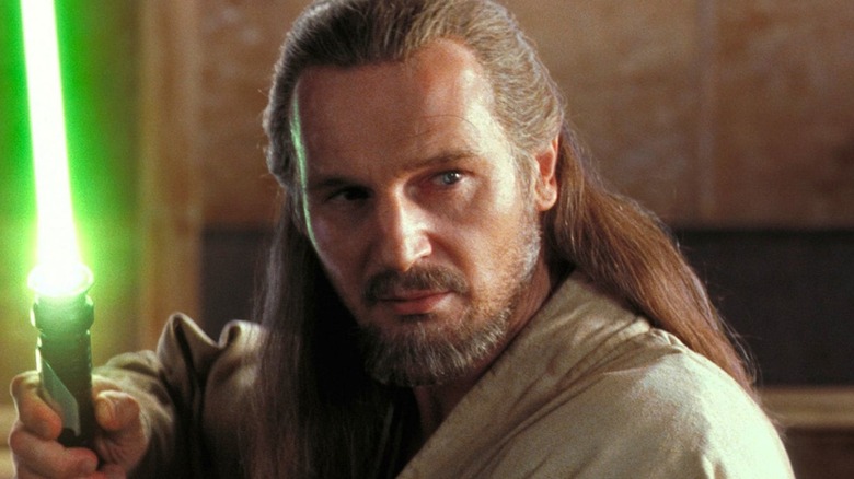 Liam Neeson as Qui-Gon Jinn brandishes a green lightsaber in close-up