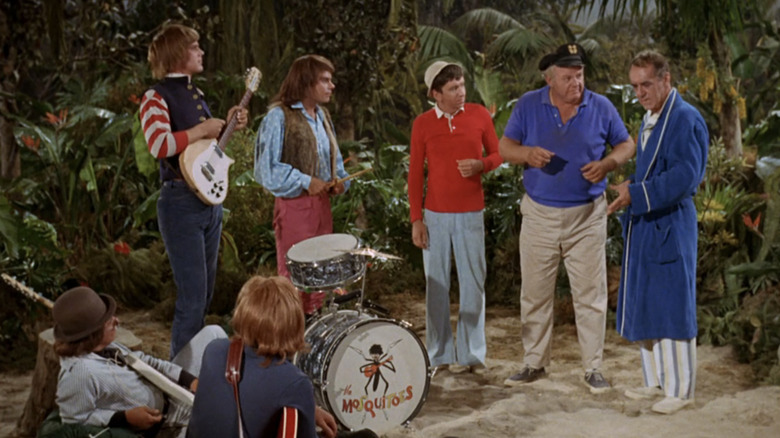 The Gilligan's Island cast stands in front of a band on a beach in Gilligan's Island