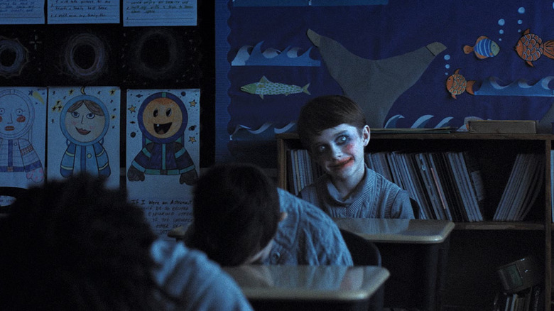 Alex smiling creepily with clown makeup on in the classroom in Weapons