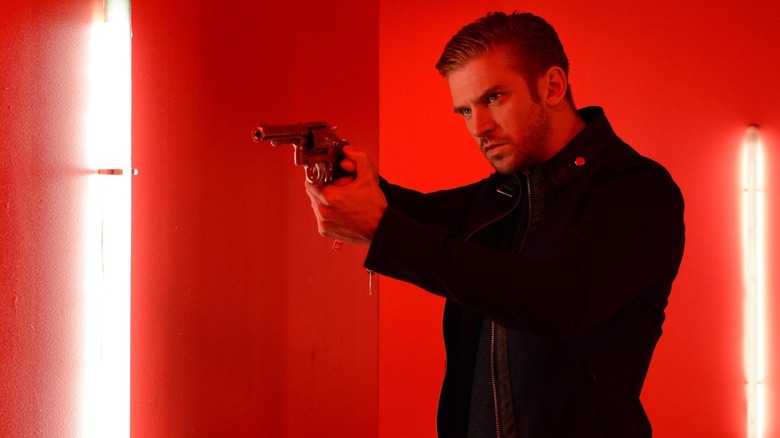 man in black holding a gun in a red room with bright white lights