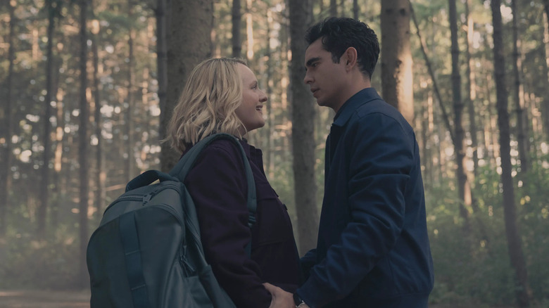 June (Elisabeth Moss) and Nick (Max Minghella) stand close in a forest, holding hands as June smiles warmly and Nick gazes at her intensely in The Handmaid's Tale