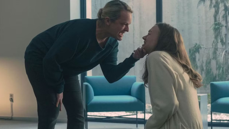 June (Elisabeth Moss) crouches down and holds the bottom of Serena's chin (Yvonne Strahovski) while screaming with rage in The Handmaid's Tale