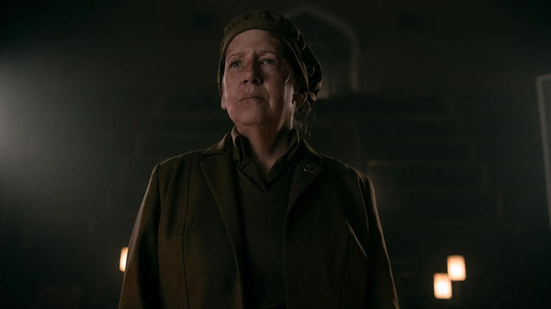 Aunt Lydia (Ann Dowd) stands tall and proud against a brick wall in a dimly-lit room in The Handmaid's Tale