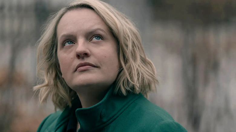 June (Elisabeth Moss) looks contemplatively up towards the sky, wearing an emerald green coat in The Handmaid's Tale