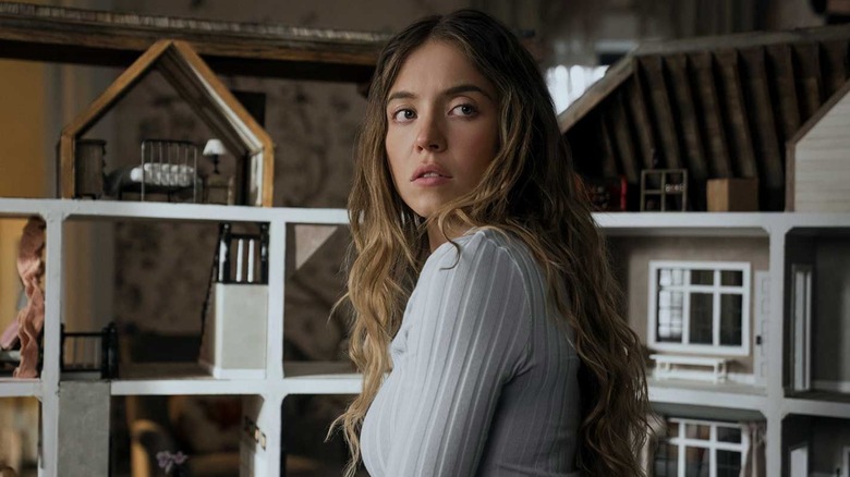 Millie looking over her shoulder in front of the dollhouse in The Housemaid