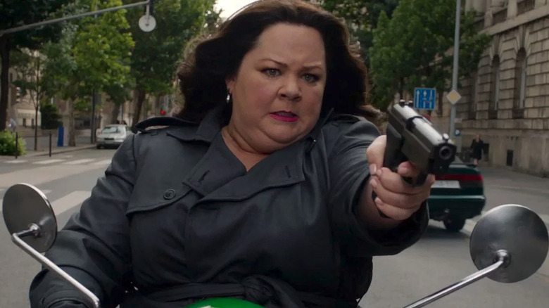 Melissa McCarthy as Susan Cooper pointing a gun on a scooter in Spy