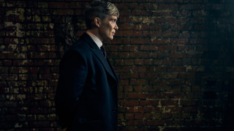 Cillian Murphy as Tommy Shelby standing next to a brick wall in Peaky Blinders: The Immortal Man