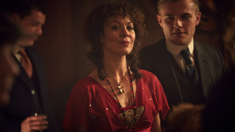 Helen McCrory as Polly Gray wearing a red dress and smirking in a crowded room in Peaky Blinders