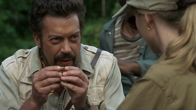 Tim Curry as Herkermer Homolka holding up a piece of treasure in Congo