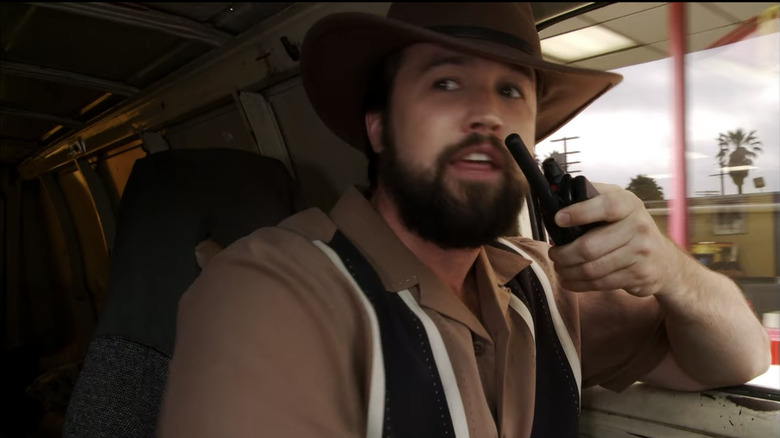 Ronald "Mac" McDonald (Rob Mac) drives a van while donning a bowling shirt and Indiana Jones hat as he speaks on a walkie talkie in "It's Always Sunny in Philadelphia"