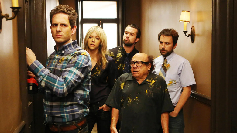 Dennis Reynolds (Glenn Howerton), Dee Reynolds (Kaitlin Olson), Mac (Rob McElhenney), Frank Reynolds (Danny DeVito), and Charlie Kelly (Charlie Day) standing together in a hallway in "It's Always Sunny in Philadelphia"