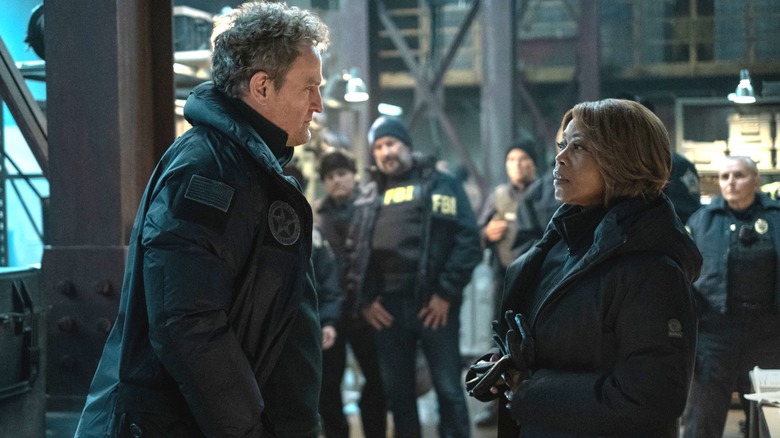 Jason Clarke as Marshal Frank Remnick and Alfre Woodard as CIA official Jacqueline Bradford standing in front of FBI agents in a warehouse in The Last Frontier