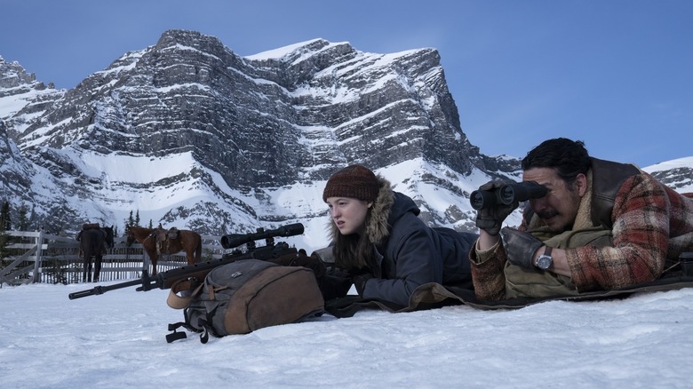 Ellie and Tommy lying in the snow with a scoped rifle in The Last of Us season 2