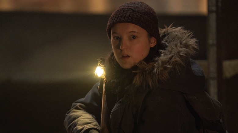 Ellie in a hat and coat, holding a shotgun and looking surprised in The Last of Us season 2