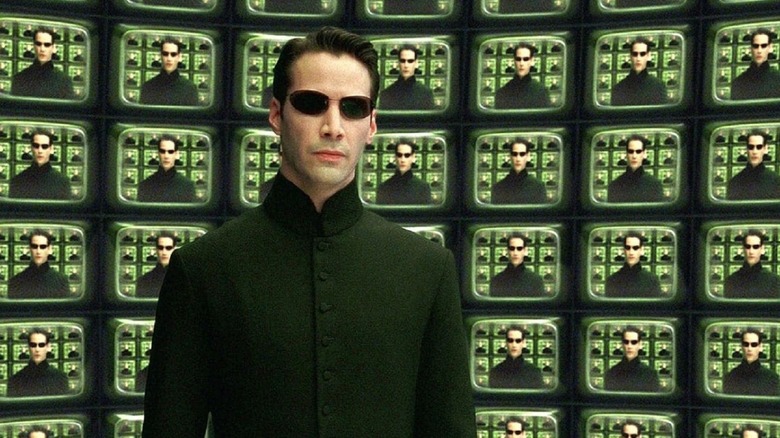 Keanu Reeves as Neo standing in front of several TV screens reflecting his image in The Matrix Reloaded