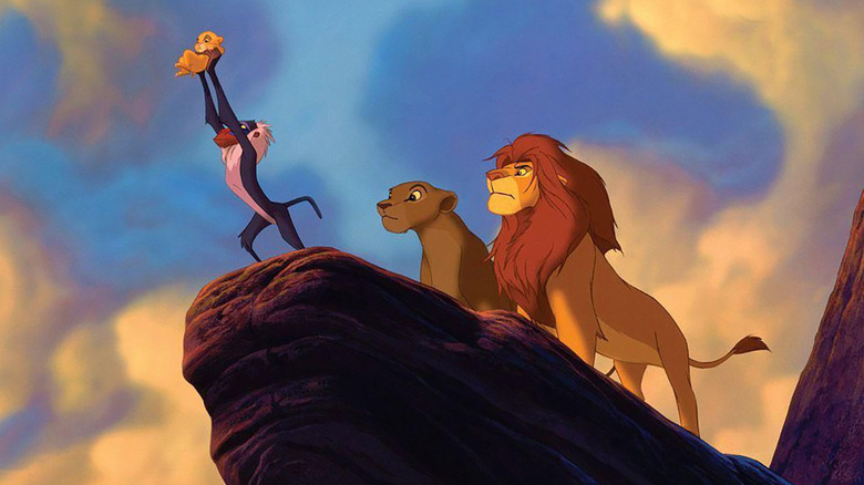 Rafiki holds up Kiara while Nala and Simba stand behind him on Pride Rock in The Lion King