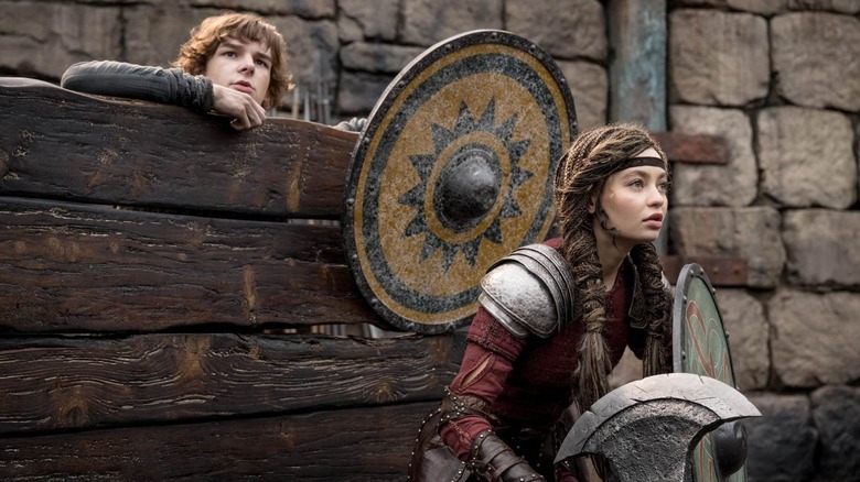 Hiccup hiding behind a fence with Astrid in front holding a shield in How to Train Your Dragon