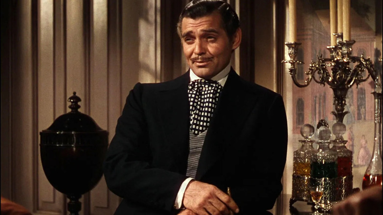 Rhett Butler, de terno, ao lado de uma bandeja de garrafas de bebida em E o Vento Levou