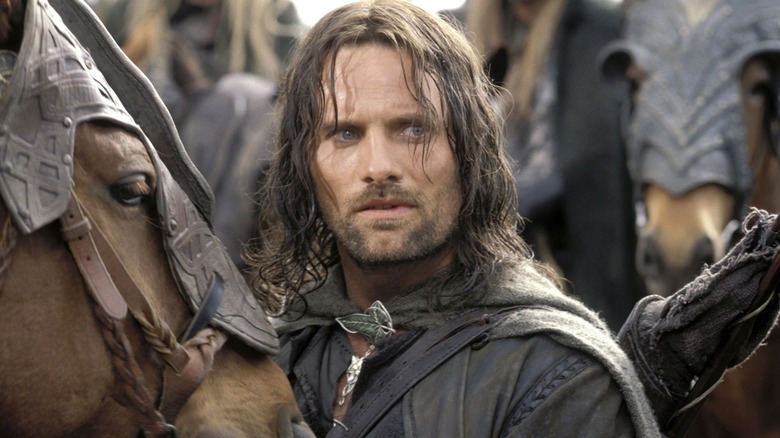 Viggo Mortensen as Aragorn standing by a horse and surrounded by other horsemen in The Lord of the Rings: The Two Towers