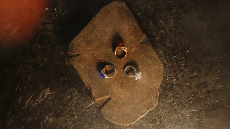 Three ornate rings, each with a different gemstone, are displayed on a flat stone in The Lord of the Rings: The Rings of Power