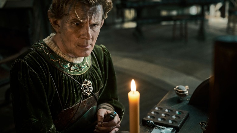 A grim-faced Celebrimbor (Charles Edwards) stands by a lit candle in The Lord of the Rings: The Rings of Power
