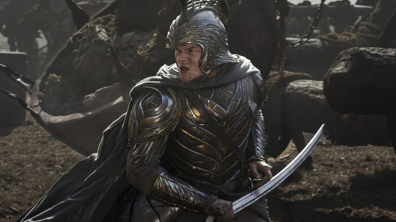 Elrond (Robert Aramayo) stands on the battlefield in armor and holding a sword in The Lord of the Rings: The Rings of Power