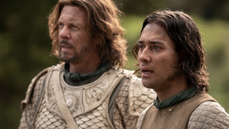 Elendil (Lloyd Owen) and Isildur (Maxim Baldry) stand shocked while wearing battle armor in The Lord of the Rings: The Rings of Power