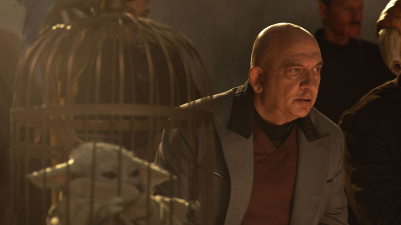 Lord Janu watching Rotta and Mando fight with Grogu in a cage by his side in The Mandalorian and Grogu