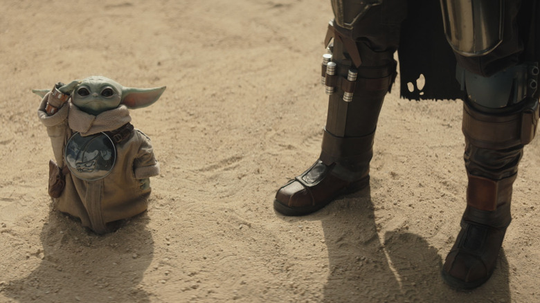 Grogu standing at Mando's feet with his armor on in The Mandalorian and Grogu