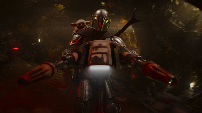 Pedro Pascal as Din Djarin riding a speeder with Grogu perched on his shoulder and droids firing blasters behind him in Star Wars: The Mandalorian and Grogu