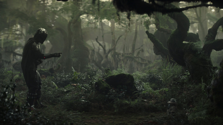 Pedro Pascal as Din Djarin gestures toward Grogu in a wild jungle in Star Wars: The Mandalorian and Grogu