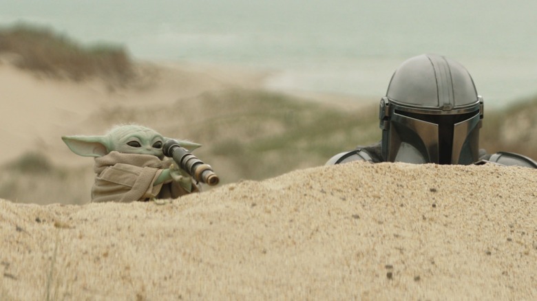 Grogu scouts an area as Din looks on in The Mandalorian and Grogu