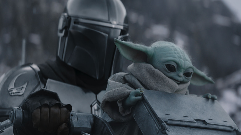 Pedro Pascal as Din Djarin in his helmet and armor riding a speeder with Grogu in Star Wars: The Mandalorian and Grogu