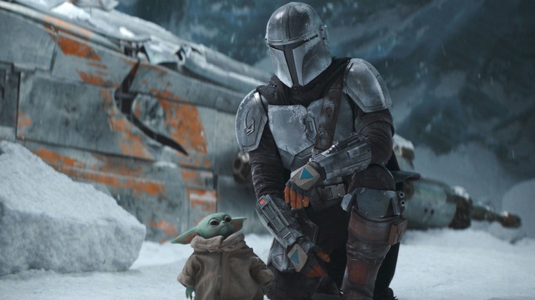a person in a metal suit kneeling next to baby yoda next to a space ship