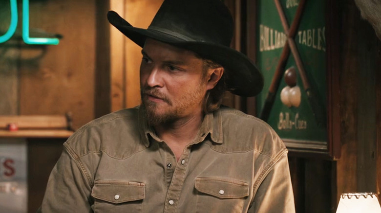 ల్యూక్ గ్రిమ్స్ 'కేస్ డటన్ మార్షల్స్‌లోని బార్‌లో నిలబడి అతని కుడివైపు చూస్తున్నాడు