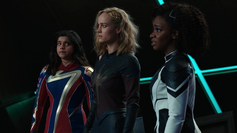 Iman Vellani's Ms. Marvel, Brie Larson's Captain Marvel, and Teyonah Parris's Monica Rambeau stand side by side against a black background in The Marvels