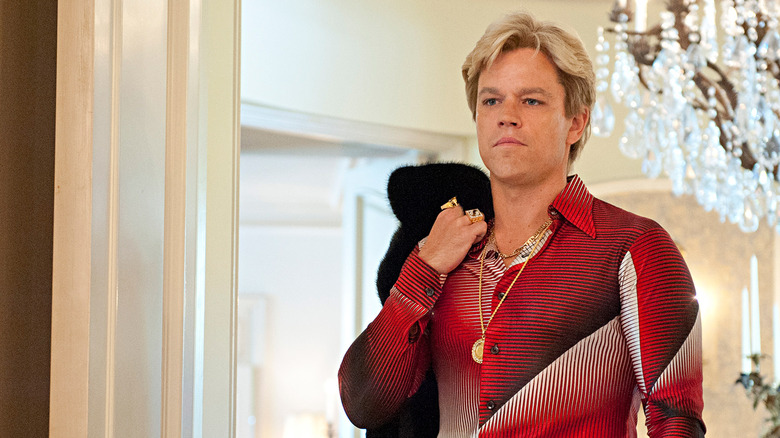 Scott Thorson holds a coat over his shoulder while dressed in gaudy 80's clothing with a gold chain in 
