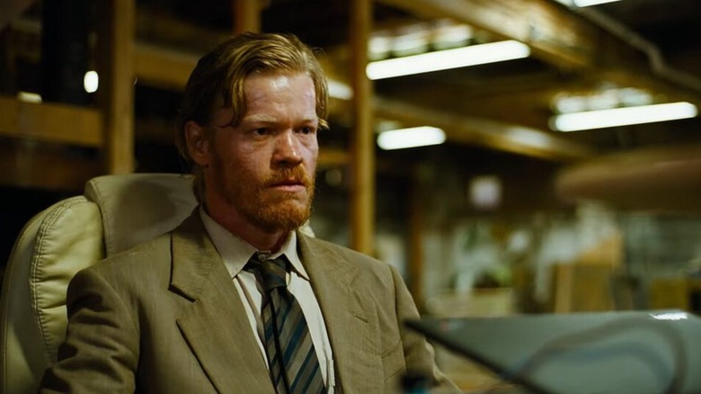 Bugonia - Teddy in suit sitting at desk with laptop