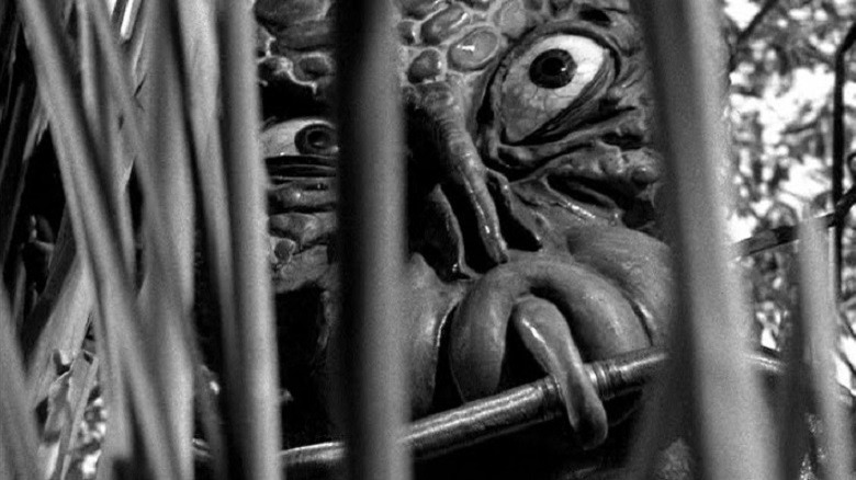 An alien peers from behind some vines