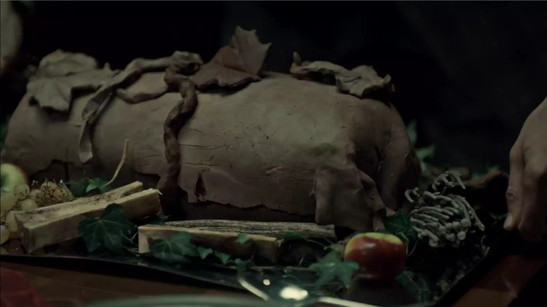 A platter covered in leaves, bones, and apples, with a clay-wrapped thigh at the center