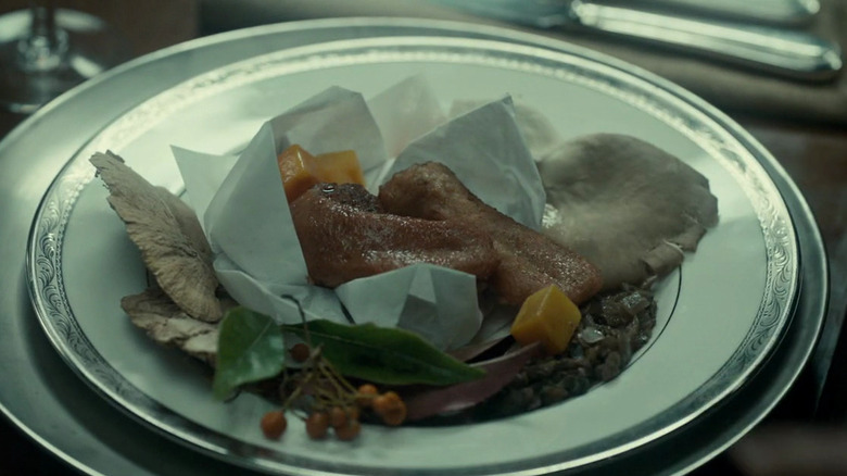 A plate covered with mushrooms, vegetables, and tongue wrapped in parchment paper