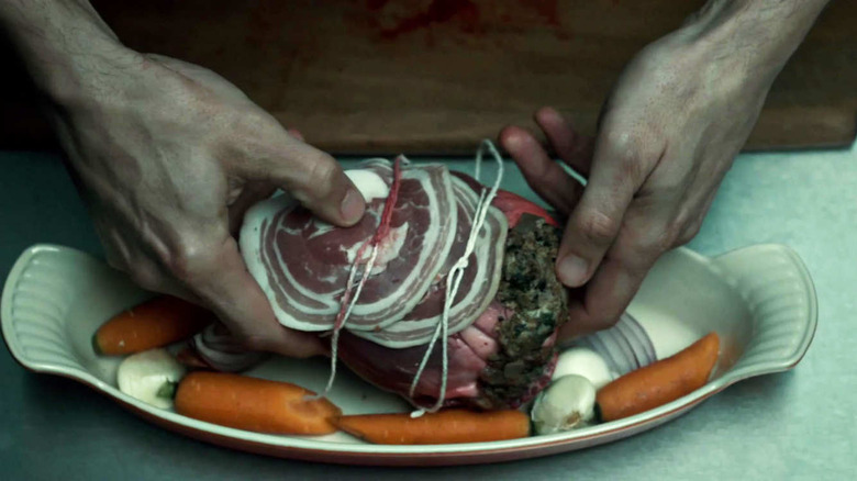 Hands prepare a raw heart, stuffed with vegetables and wrapped in pancetta