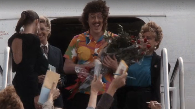 Weird Al Yankovic receives flowers, press, and fans while exiting a passenger plane in The Naked Gun (1988)
